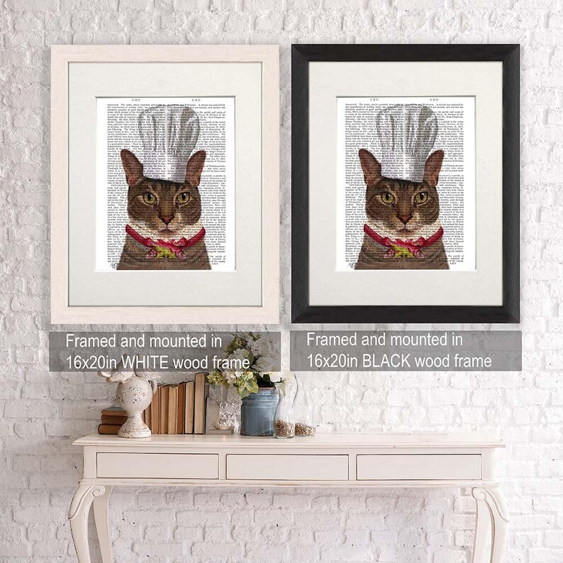 May include: Two framed prints of a cat wearing a chef's hat. The cat is brown with green eyes. The print on the left is framed in white and the print on the right is framed in black. Both frames are 16x20 inches.