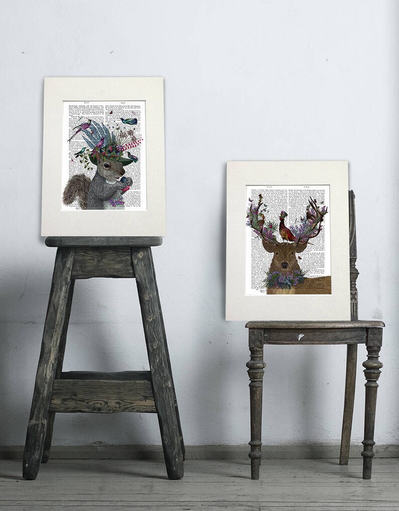 Puede incluir: Dos impresiones enmarcadas de ilustraciones de animales con acentos florales y de p&aacute;jaros. La primera impresi&oacute;n presenta una ardilla con un sombrero con flores y p&aacute;jaros. La segunda impresi&oacute;n presenta un ciervo con cuernos adornados con flores y un p&aacute;jaro.