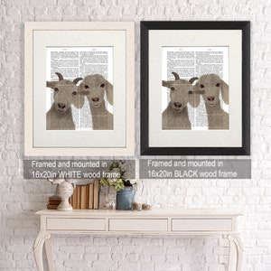 May include: Two framed prints of goats with their heads together, one with a white frame and the other with a black frame. The prints are mounted on a white wall above a white table with a vase of flowers and books.