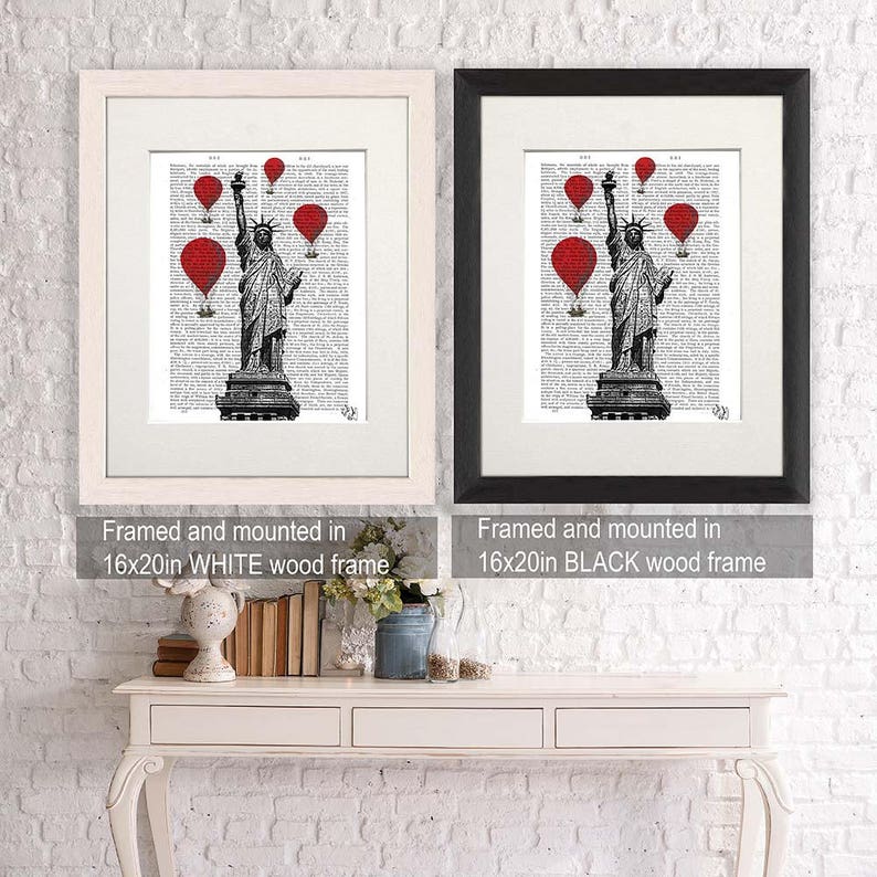 May include: A black and white illustration of the Statue of Liberty with red hot air balloons in the background. The image is framed in a white wood frame and a black wood frame. The text "Framed and mounted in 16x20in WHITE wood frame" and "Framed and mounted in 16x20in BLACK wood frame" is below each image.