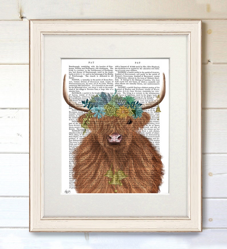 May include: A Highland cow with a floral crown made of succulents and flowers. The cow is brown and has a white face. The background is a vintage book page with text.