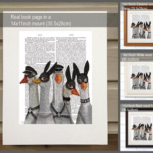 May include: Five white geese wearing black leather masks and harnesses. The geese are arranged in a row, with the one in the center wearing a bunny mask. The image is printed on a book page with text in the background. The image is framed in a white wood frame.