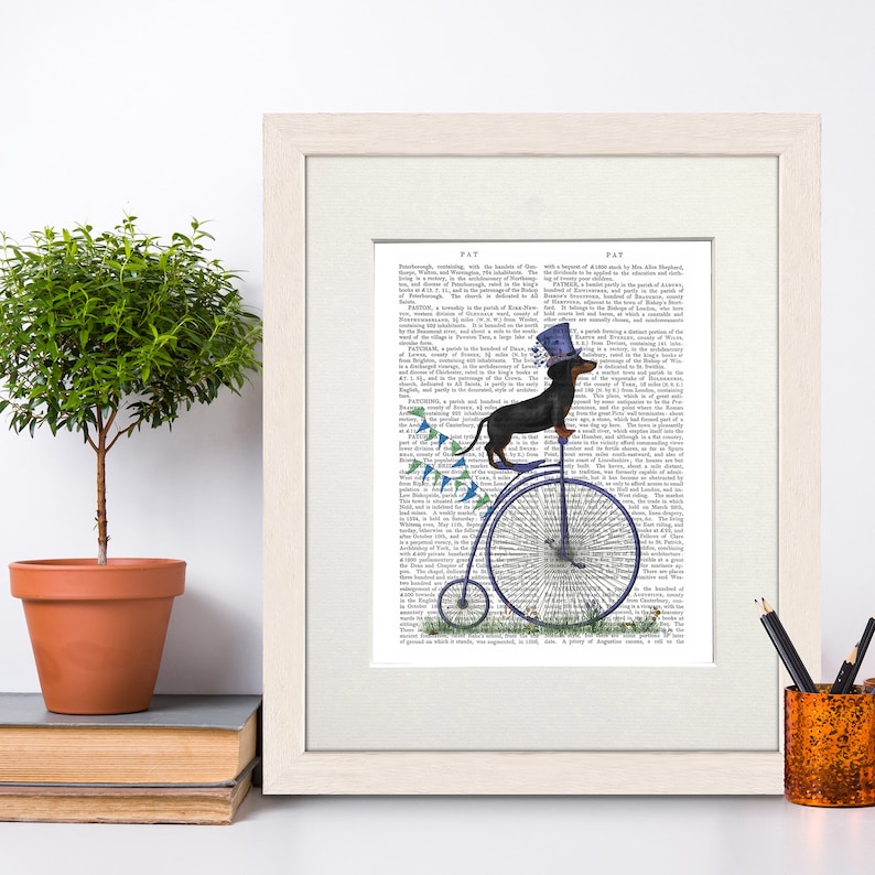 May include: A black and tan dachshund wearing a blue top hat and riding a penny-farthing bicycle. The bicycle has a blue frame and a large front wheel. The background is a vintage book page with text.