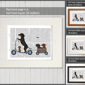 May include: A black and tan dachshund dog riding a scooter with two smaller dachshund dogs in a wagon behind it. The image is printed on a book page and framed in a white wood frame. The frame is 14 inches by 11 inches (35.5 cm by 28 cm).