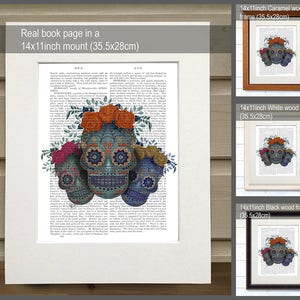 May include: Three colorful sugar skulls with floral accents on a book page with text. The skulls are blue, green, and purple with intricate designs. The flowers are pink, orange, and yellow. The book page is a vintage style with a white background and black text. The image is framed in a 14x11 inch mount.
