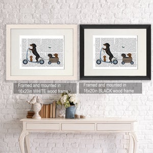 May include: A framed print of a black and brown dachshund riding a scooter with two smaller dachshunds in a wagon. The print is on a white background with black text. The frame is white and measures 16x20 inches.