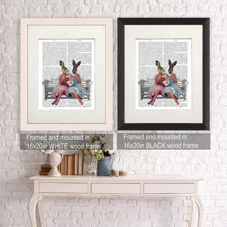 May include: Two framed prints of a vintage illustration of two rabbits wearing dresses and hats, sitting on a bench and drinking tea. The prints are framed in white and black wood frames. The text on the frames reads "Framed and mounted in 16x20in WHITE wood frame" and "Framed and mounted in 16x20in BLACK wood frame".