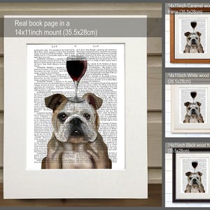 May include: A bulldog with a glass of red wine on its head, printed on a book page. The image is framed in a white, black, and caramel wood frame. The frame is 14 inches by 11 inches, or 35.5 centimeters by 28 centimeters.