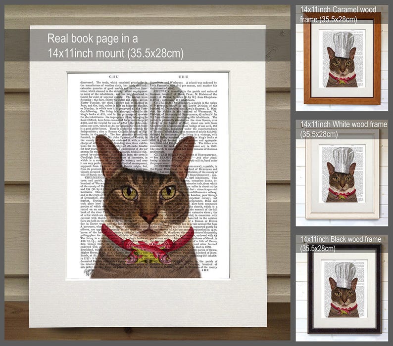 May include: A brown tabby cat wearing a white chef's hat and a red and white ribbon around its neck. The cat is printed on a book page with text. The image is framed in a black wood frame. The image is also available in white and caramel wood frames.