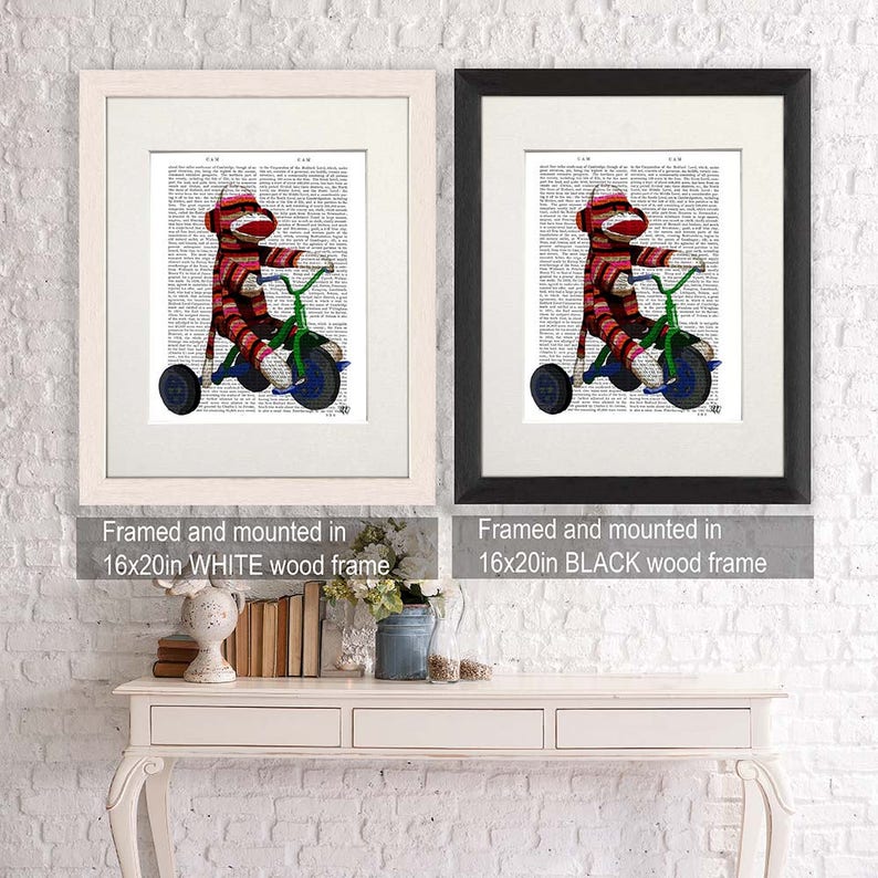 May include: Two framed prints of a sock monkey riding a tricycle on a vintage book page background. The frames are 16x20 inches and are shown in white and black.