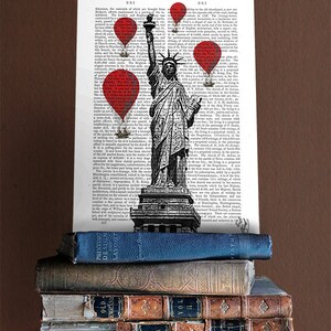 May include: A black and white illustration of the Statue of Liberty with red balloons floating above it. The illustration is printed on a page of a vintage book with text in black and white. The book is stacked on top of other vintage books.