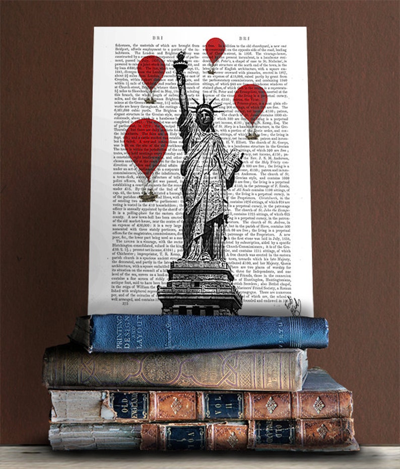 May include: A black and white illustration of the Statue of Liberty with red balloons floating above it. The illustration is printed on a page of a vintage book with text in black and white. The book is stacked on top of other vintage books.