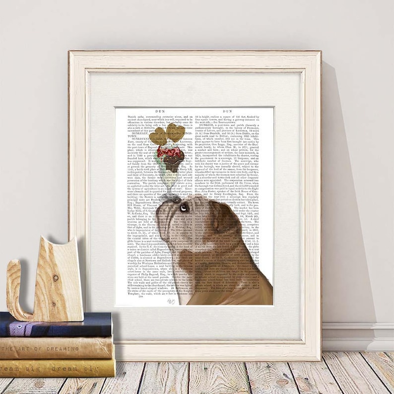 May include: A framed print featuring a brown bulldog looking up at a sundae with heart-shaped toppings. The artwork is set against a vintage dictionary page background, framed in a white wooden frame.