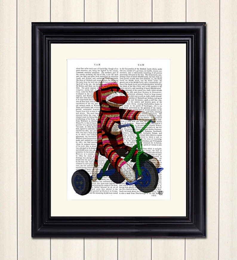 May include: A red and white striped sock monkey riding a green tricycle on a page of a vintage book. The book page has text about the history of Cambridge, England.