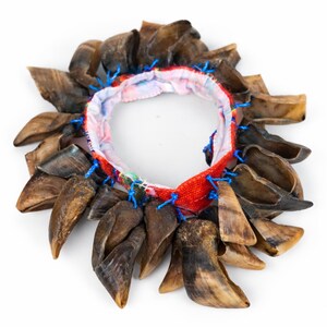 Puede incluir: Un collar &uacute;nico con una banda de tela roja y estampada, adornado con numerosos colgantes marrones en forma de pezu&ntilde;a. Los colgantes est&aacute;n sujetos con hilo azul, creando un contraste llamativo con la colorida banda.