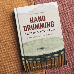 Pode incluir: Um livro intitulado "Hand Drumming Getting Started" com uma imagem de bateria na capa. O livro é uma primeira edição canadense e inclui áudio de acompanhamento. A capa apresenta um close-up de uma bateria com detalhes marrons e pretos.