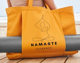 May include: Mustard yellow tote bag with a yoga mat. The bag features a black line drawing of a person in a yoga pose with the word "NAMASTE" and the city "FLORENCE" printed below. The yoga mat is gray.