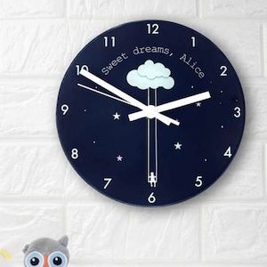 May include: A blue round clock with white hands and numbers. The clock face has a white cloud with a girl swinging from it. The text "Sweet dreams, Alice" is written on the clock face.