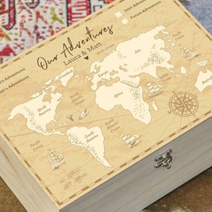 May include: A wooden box with a map of the world on the lid. The map is in a vintage style and includes the names of continents and oceans. The box has a silver latch and is labeled "Our Adventures Laura & Matt".