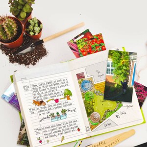May include: A green and white journal with a hand-drawn garden plan and notes about planting dates and types of plants. The journal is open to a page with a hand-drawn garden plan with a pond, lawn, and a house. The journal is surrounded by gardening tools, plants, and photos.
