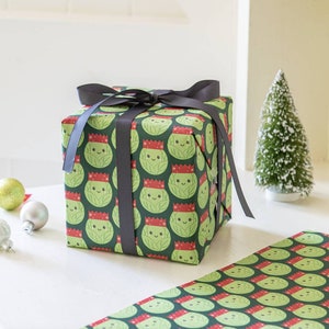 Pode incluir: Um papel de embrulho verde e vermelho com um padr&atilde;o de br&oacute;colis de desenho animado usando chap&eacute;us de Papai Noel. O presente &eacute; embrulhado com uma fita preta.