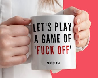 May include: White ceramic mug with the text "LET'S PLAY A GAME OF 'FUCK OFF'" in black and red lettering. The phrase "YOU GO FIRST" is printed below the main text. The mug is held by a person against a red background.