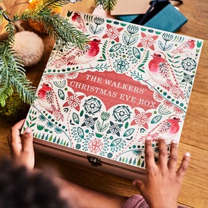 May include: A wooden Christmas Eve box with a red, green and white floral design. The box has a hinged lid and a metal clasp. The text "The Walkers' Christmas Eve Box" is printed on the front of the box.