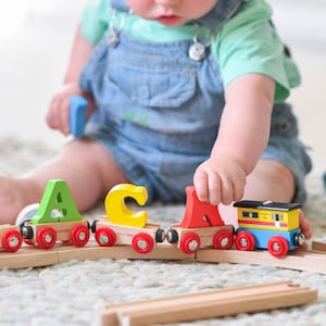 May include: A wooden toy train with colourful letter blocks spelling out the word "ACA" and a yellow and blue train car with the text "Freight Train" on the side.