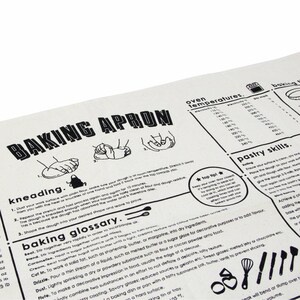 Puede incluir: Delantal de cocina blanco y negro con ilustraciones de amasar la masa y una tabla de temperaturas del horno. El texto "Baking Apron" est&aacute; en letras grandes y negritas en la parte superior del delantal. El delantal tambi&eacute;n incluye un glosario de t&eacute;rminos de reposter&iacute;a.