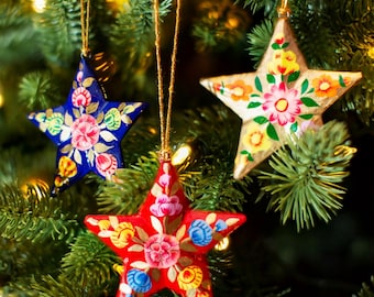 May include: Three hand-painted paper star ornaments with floral designs. The stars are blue, red, and gold with white and yellow accents.