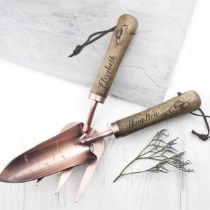 May include: Two gardening tools with wooden handles. The handles are engraved with the names "Elizabeth" and "Hamilton". The tools are made of copper and have a trowel and a cultivator.