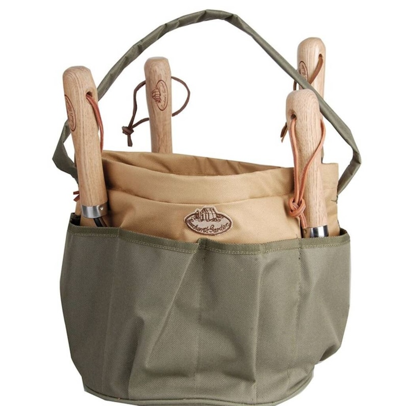 K&ouml;nnte beinhalten: Eine Gartentasche aus olivgr&uuml;nem und beigefarbenem Canvas mit Griff und mehreren Taschen. Sie enth&auml;lt vier Gartenger&auml;te mit Holzgriffen und Lederschlaufen. Die Tasche hat ein Etikett mit der Aufschrift "Orchard & Garden".