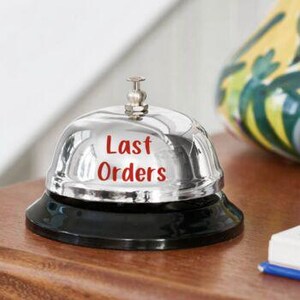 Puede incluir: Una campana cromada brillante con una base negra. Las palabras "Last Orders" est&aacute;n impresas en rojo en la superficie de la campana. La campana est&aacute; sobre una superficie de madera.