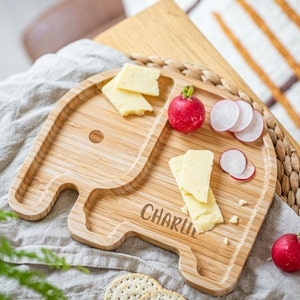 Può includere: Un piatto di legno a forma di elefante con due sezioni, una per il formaggio e l'altra per i ravanelli a fette. Il piatto è personalizzato con il nome "Charlie".