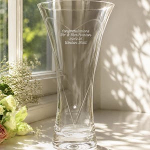 May include: A clear glass vase with a flared rim and a tapered base. The front features an etched heart outline, a single embedded crystal accent, and the engraved text: Congratulations Mr & Mrs Pointon 09.12.26 Weston Hall.