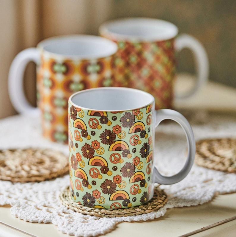 May include: Three ceramic mugs with retro designs. The mugs feature a green background with peace signs, flowers, and rainbows. The mugs are perfect for adding a touch of vintage style to your kitchen.