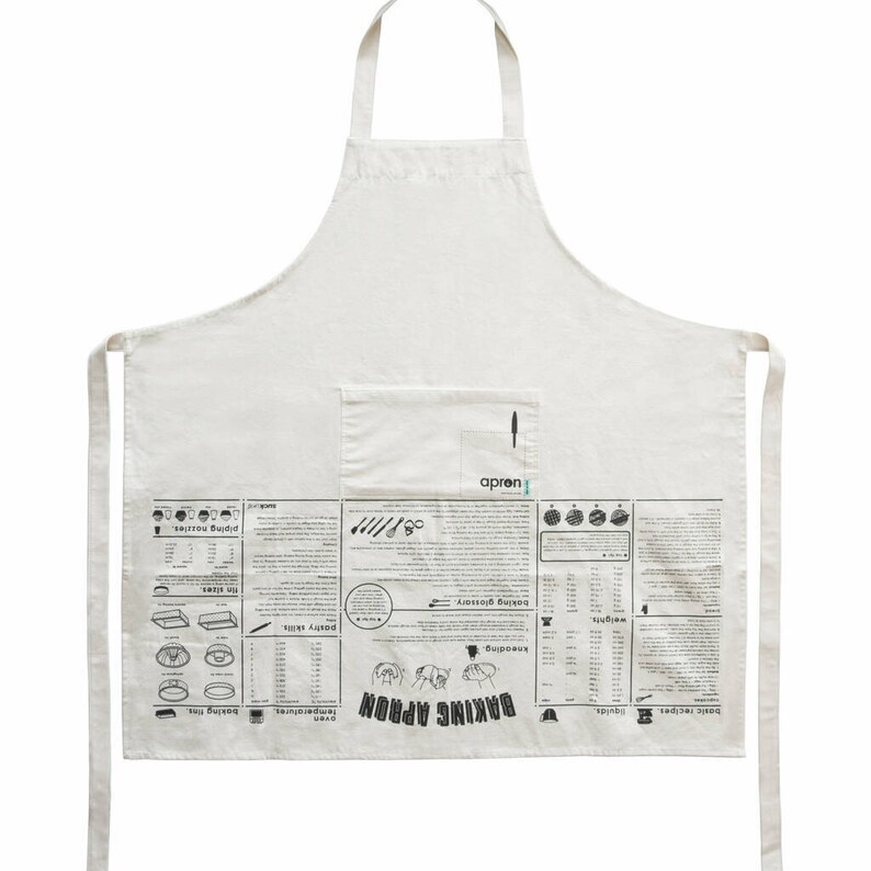 Puede incluir: Un delantal de algod&oacute;n blanco con un bolsillo grande en la parte delantera. El delantal tiene un estampado en blanco y negro de t&eacute;rminos y herramientas de reposter&iacute;a, incluyendo "Baking Apron", "temperatures", "baking times", "kneading", "pastry skills", "baking glossary", y "piping nozzles".
