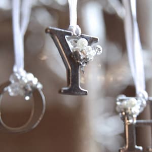 May include: Silver letter Y ornament with white beads hanging from a white ribbon.
