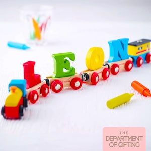 May include: A wooden toy train set with colourful carriages carrying the letters L, E, O, and N. The engine is red and yellow, followed by carriages with a red L, green E, yellow O, and blue N, ending with a yellow and blue caboose on red wheels.
