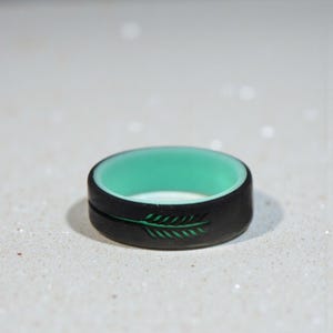May include: A black silicone ring with a teal interior. The exterior features a green arrow design. This ring is a stylish accessory for everyday wear.