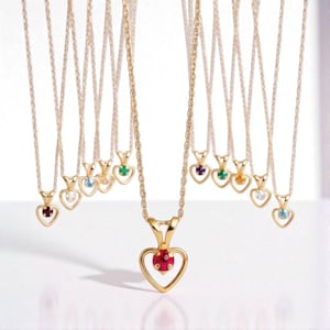 May include: A collection of gold-colored necklaces with heart-shaped pendants, each featuring a different colored gemstone. The gemstones include red, white, blue, green, purple, and yellow. The necklaces hang against a white background.