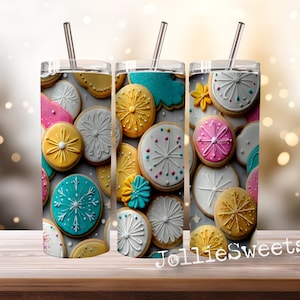 Può includere: Tre bicchieri in acciaio inossidabile con coperchi e cannucce, con un design di biscotti colorati con vari disegni di glassa. I bicchieri sono su una superficie di legno.