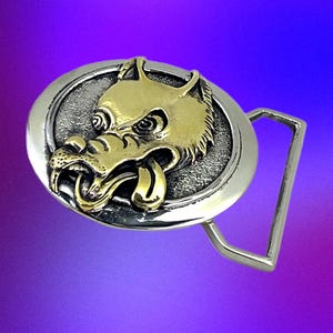 May include: A silver and gold-toned metal belt buckle featuring a detailed wolf head design. The wolf's head is gold, with a silver textured background and a silver buckle frame. The wolf has its tongue sticking out.