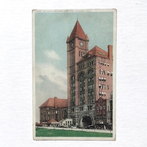 May include: A vintage postcard depicting the Illinois Central Station in Chicago, Illinois. The postcard features a large, brick building with a clock tower and a large arched entrance. The building is surrounded by a grassy area and a few trees.