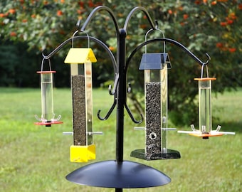 May include: Four bird feeders hanging from a black metal stand. The feeders are clear plastic tubes with different colored tops. The feeders are filled with birdseed.