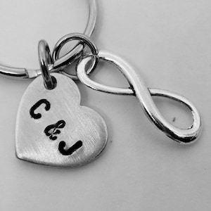 May include: Silver heart-shaped keychain with the initials "C & J" engraved on it, attached to a silver infinity symbol charm and a silver key ring.