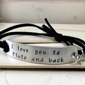 May include: A black suede bracelet with a silver charm that reads "I love you to Pluto and back".