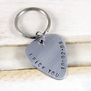 May include: A silver-colored guitar pick keychain with the words "I PICK YOU" and the date "10.02.09" engraved on it. The keychain has a silver ring attached to the top of the pick.