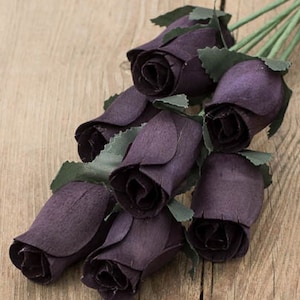May include: A bouquet of six dark purple wooden roses with green leaves. The roses are arranged in a cluster, with the stems extending out from the center.