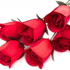 May include: A bouquet of six red wooden roses. The roses are arranged in a cluster with their stems pointing towards the right side of the image.